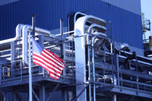 Image of an American flag in front of a factory. Manufacturers are taking out pharma equipment loans to expand.